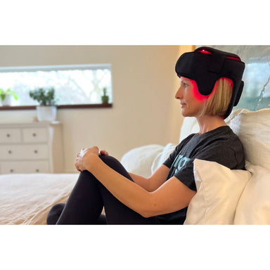 Person wearing a black Fringe Red Light Therapy Head Wrap with LED lights in a bedroom setting.