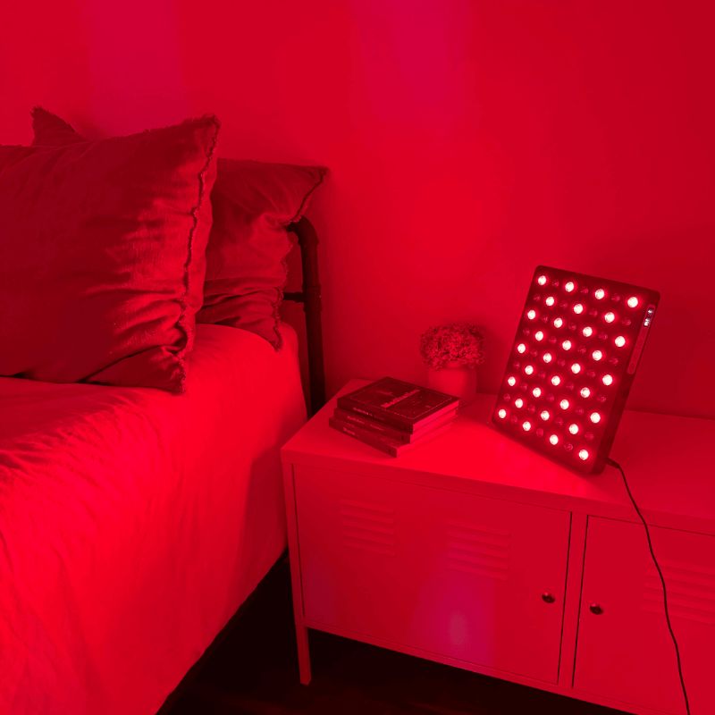 Bedroom with red lighting, bed, nightstand, and Fringe Red Light Panel