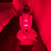 Person sitting on a chair with a Fringe Red Light Panel on their back in a dimly lit room.