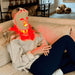 Person sitting on a couch with a Fringe Red Light Therapy Face Mask in a living room setting.