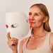 Woman holding a Therabody Theraface LED Mask
with visible red light.