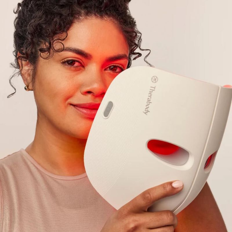 Woman holding a white Therabody Theraface LED Mask.